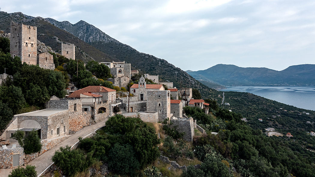 An old stone village nestled among rugged mountains overlooking a serene body of water.