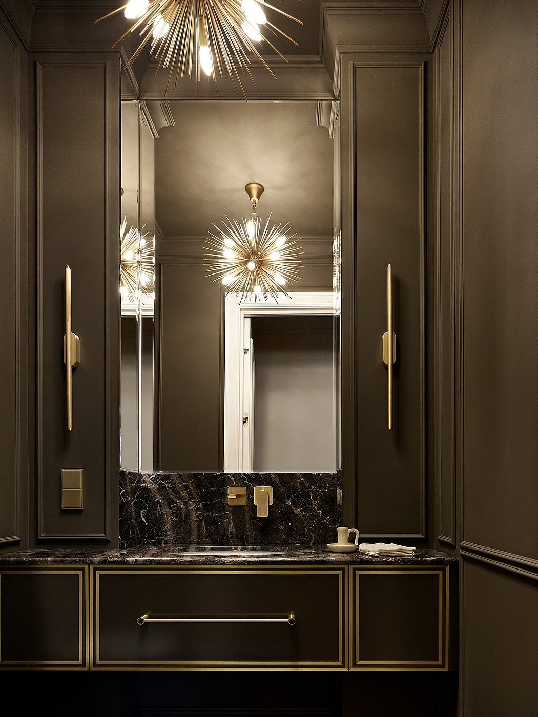 Opulent bathroom interior with elegant gold light fixtures, black marble vanity, and ornate mirror.