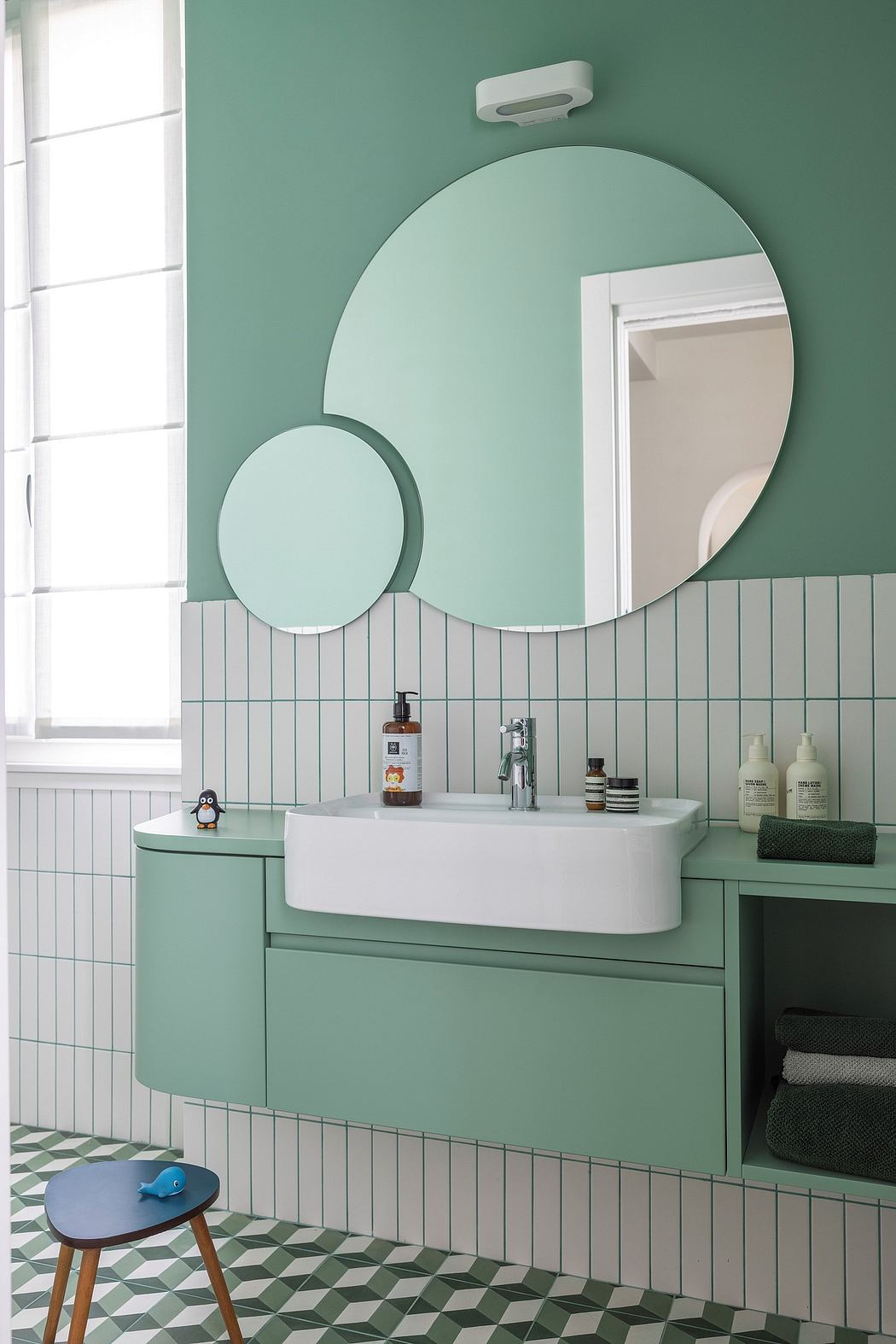 Stylish mint-green bathroom with round mirrors, tiled walls, and a modern vanity.
