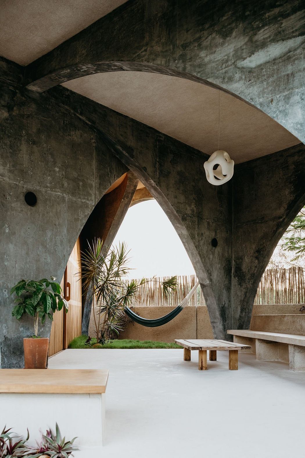 An arched concrete structure frames a lush, natural outdoor space with a hammock and wooden furniture.