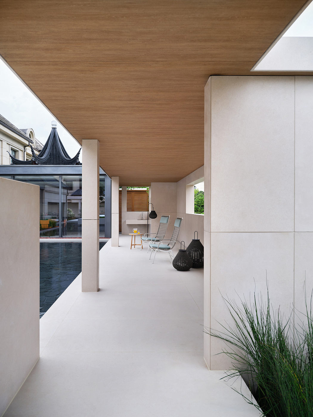 Minimalist exterior with wooden ceiling, glass walls, and sleek outdoor furniture.