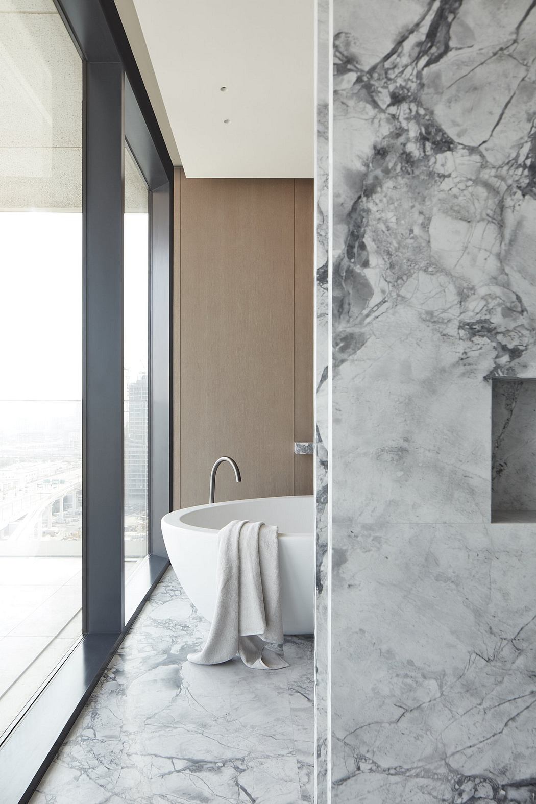 A modern, minimalist bathroom with a freestanding bathtub, marble tiles, and large windows.