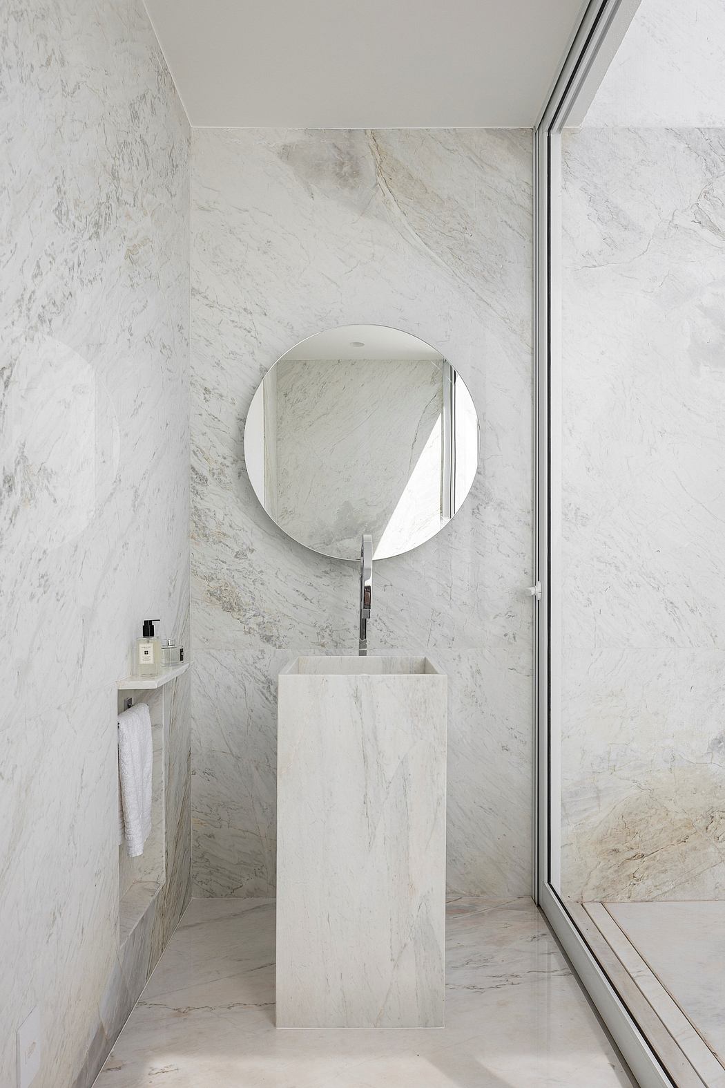 A minimalist bathroom with a round mirror, freestanding sink, and floor-to-ceiling marble cladding.