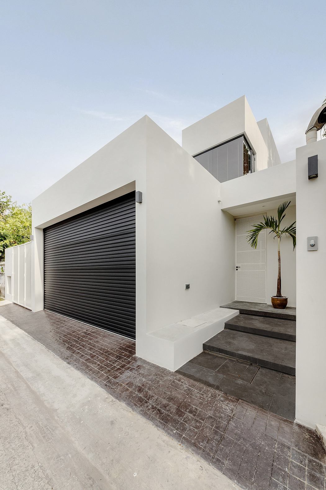 Modern two-story white house with a black garage door and a potted plant.