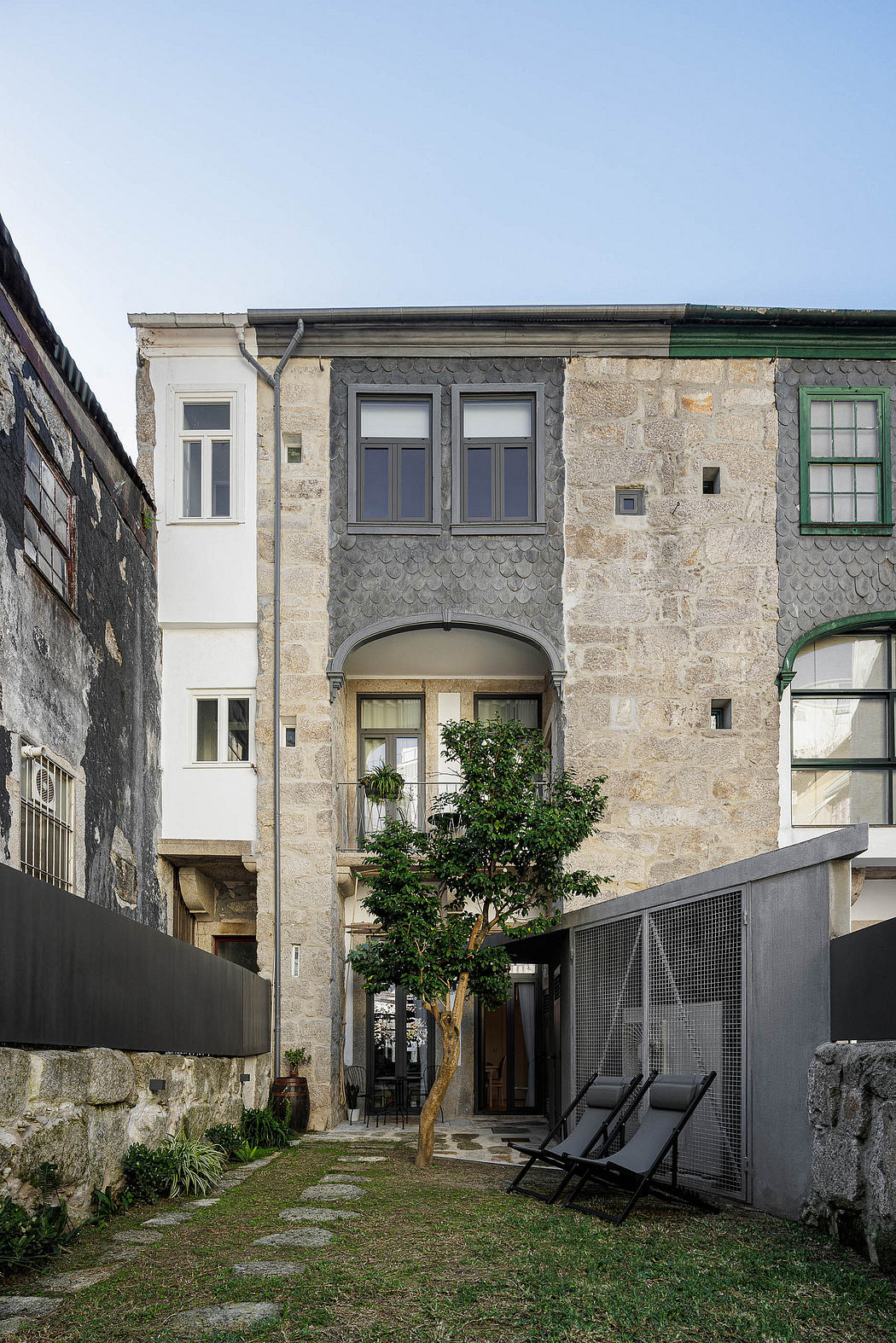 Renovated traditional building with a modern glass balcony and a courtyard with chairs.