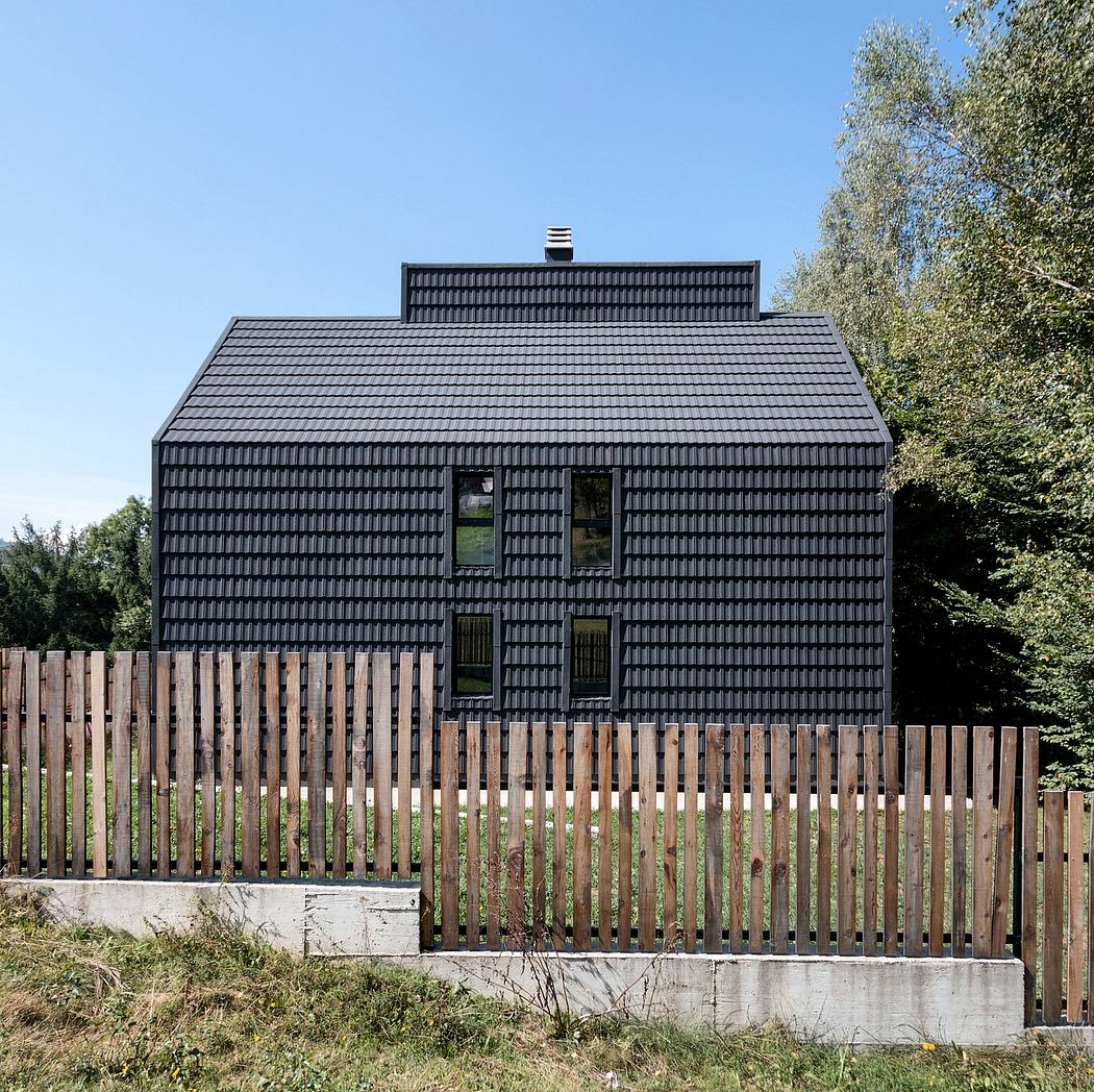 A two-story black tiled house with a wooden fence in a rural setting.