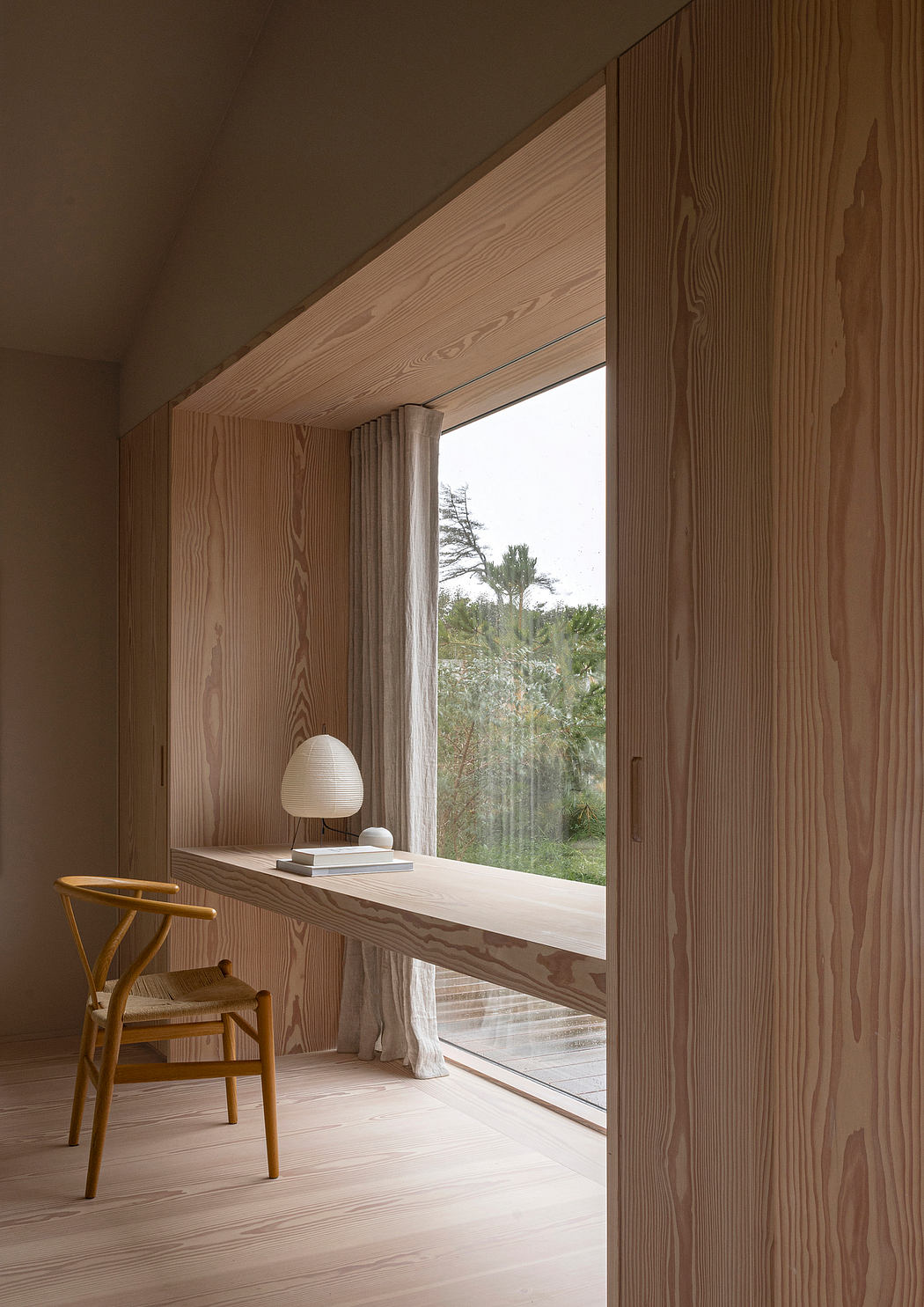 Minimalist wooden interior with a window seat and a lamp.