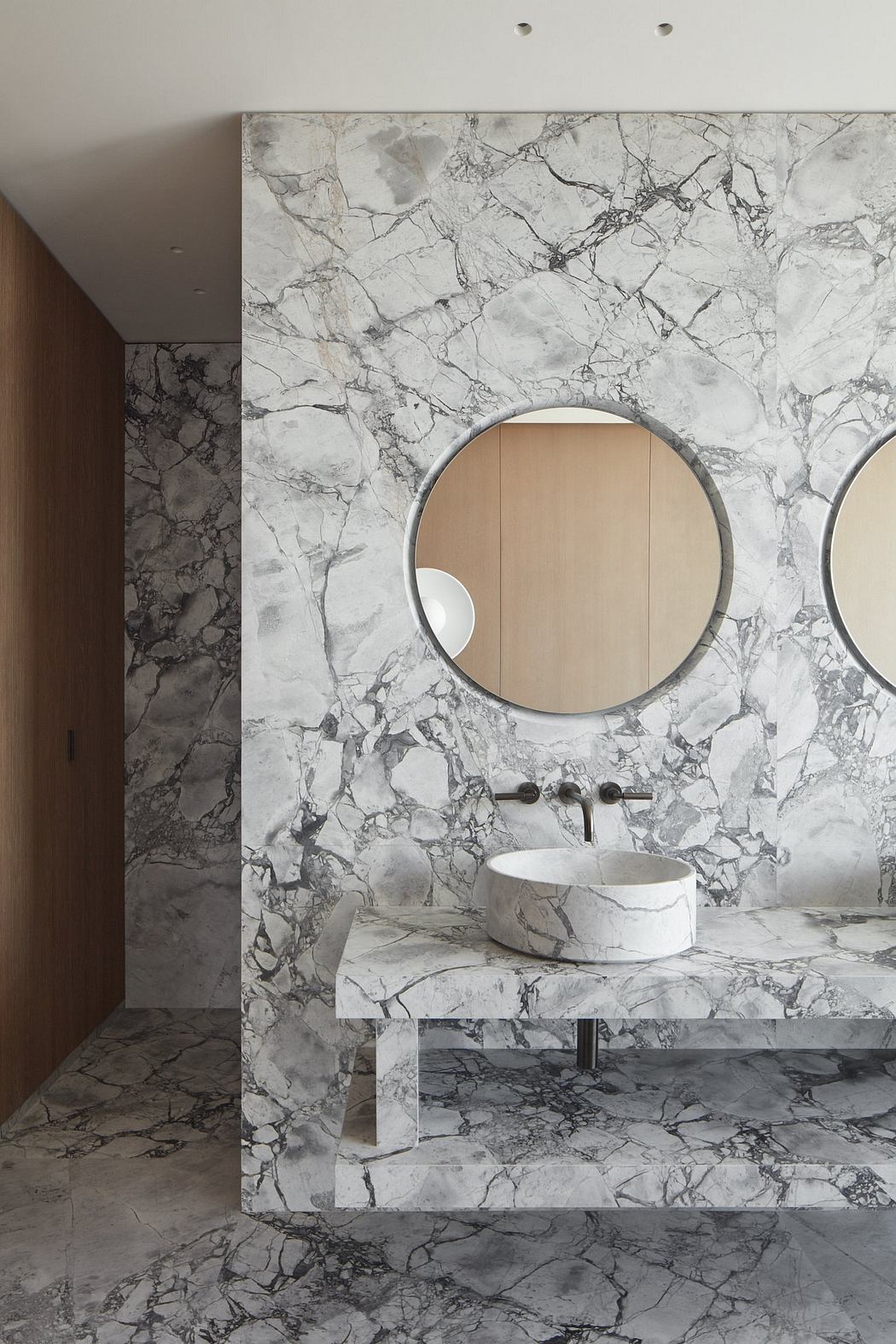 A minimalist bathroom with a marble-clad walls, round mirror, and vessel sink on a floating vanity.