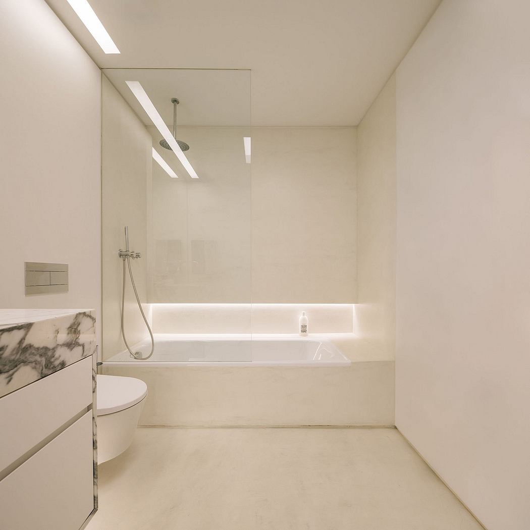 Modern, minimalist bathroom with sleek, white tiled walls, recessed lighting, and a large soaking tub.