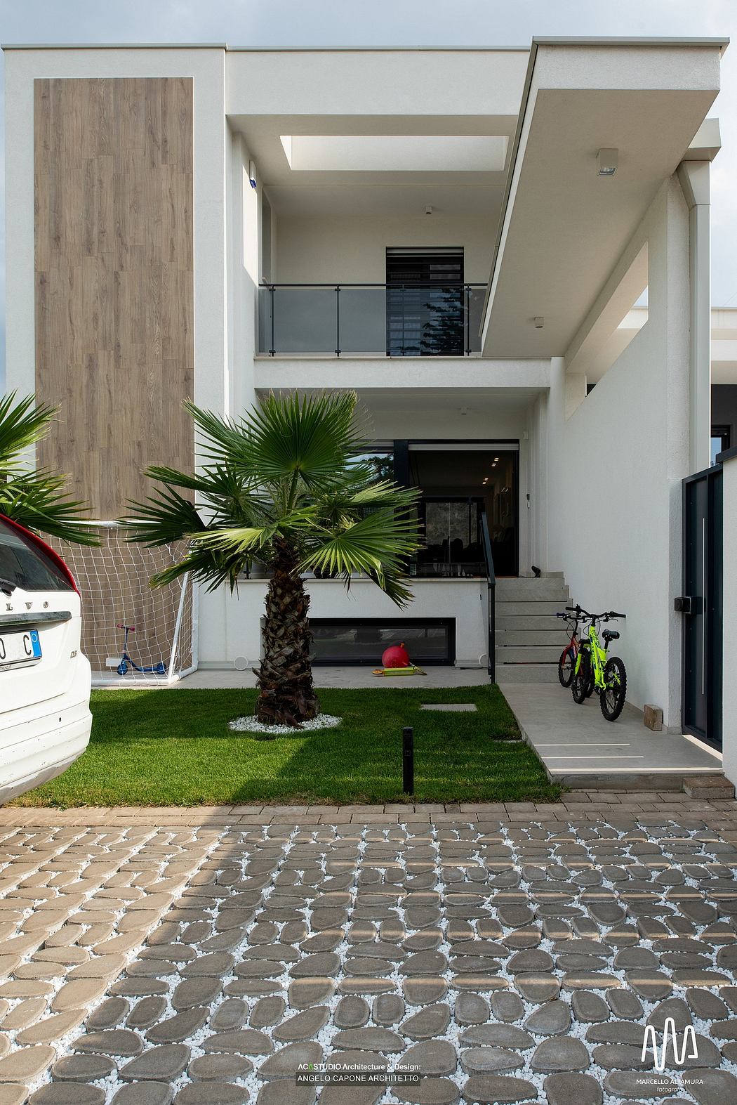 Contemporary home facade with wood paneling, palm trees, and paved outdoor space.