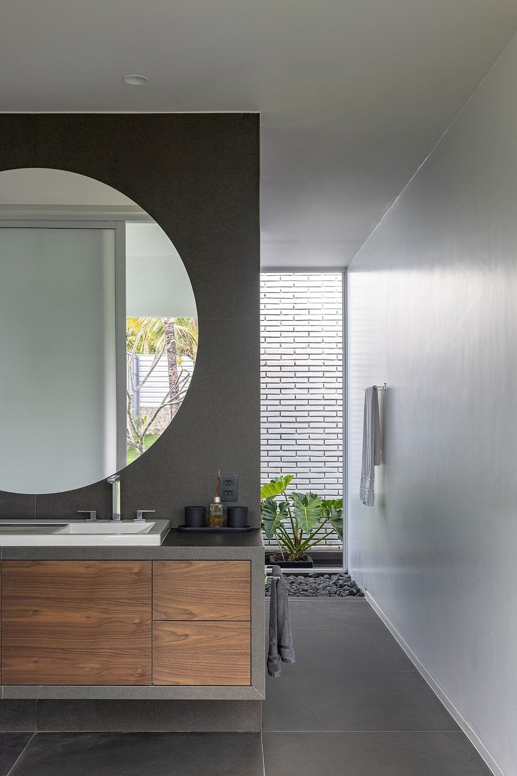 Sleek modern bathroom with wooden vanity, round mirror, and textured accent wall.