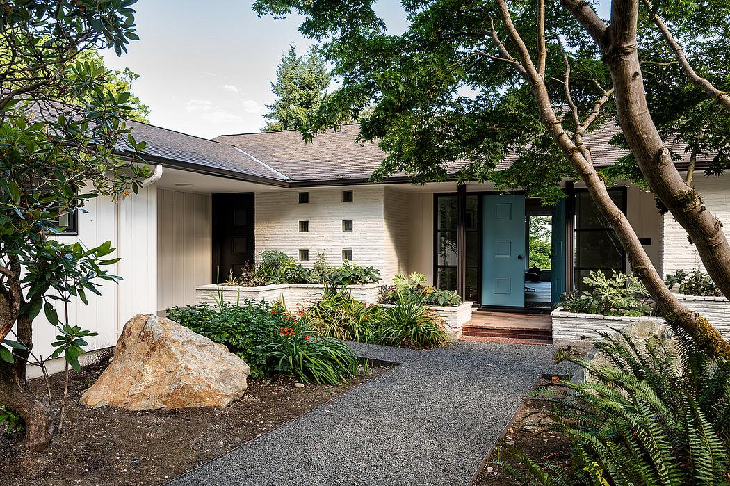 A mid-century style home with a well-designed landscape featuring a gravel pathway, lush greenery, and a vibrant teal front door.