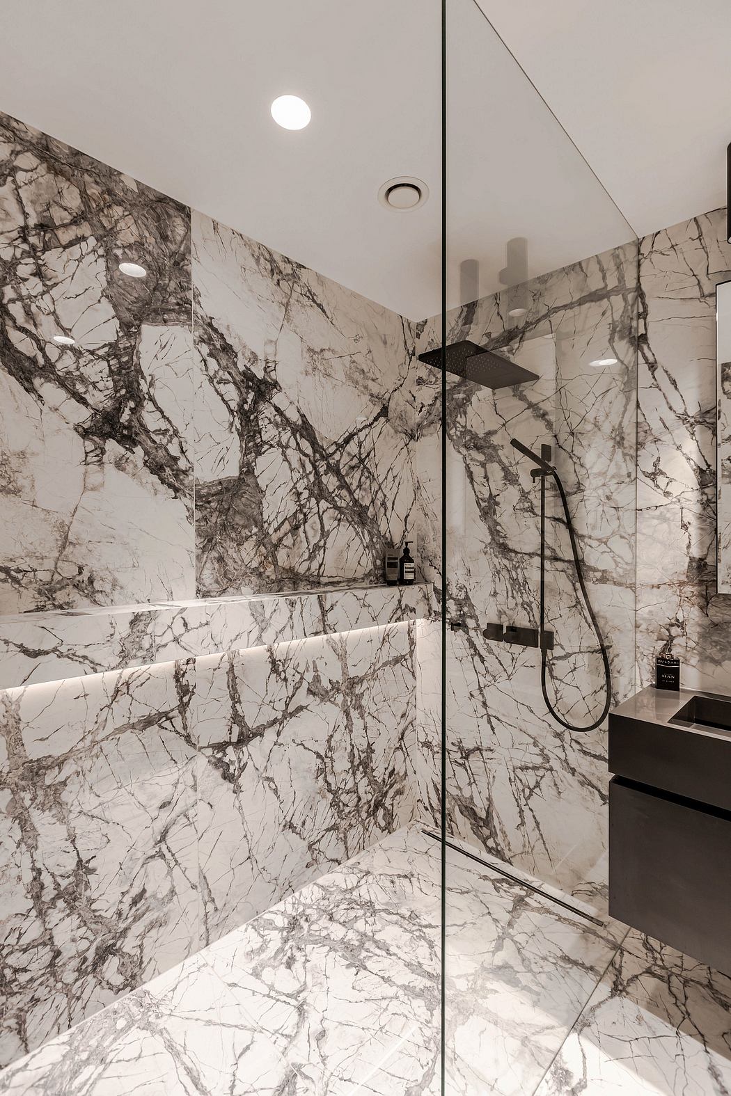 Modern bathroom with marble walls and glass shower enclosure.