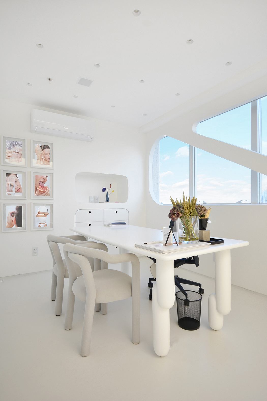 Modern, minimalist workspace with sleek white furniture, artwork, and potted plant.