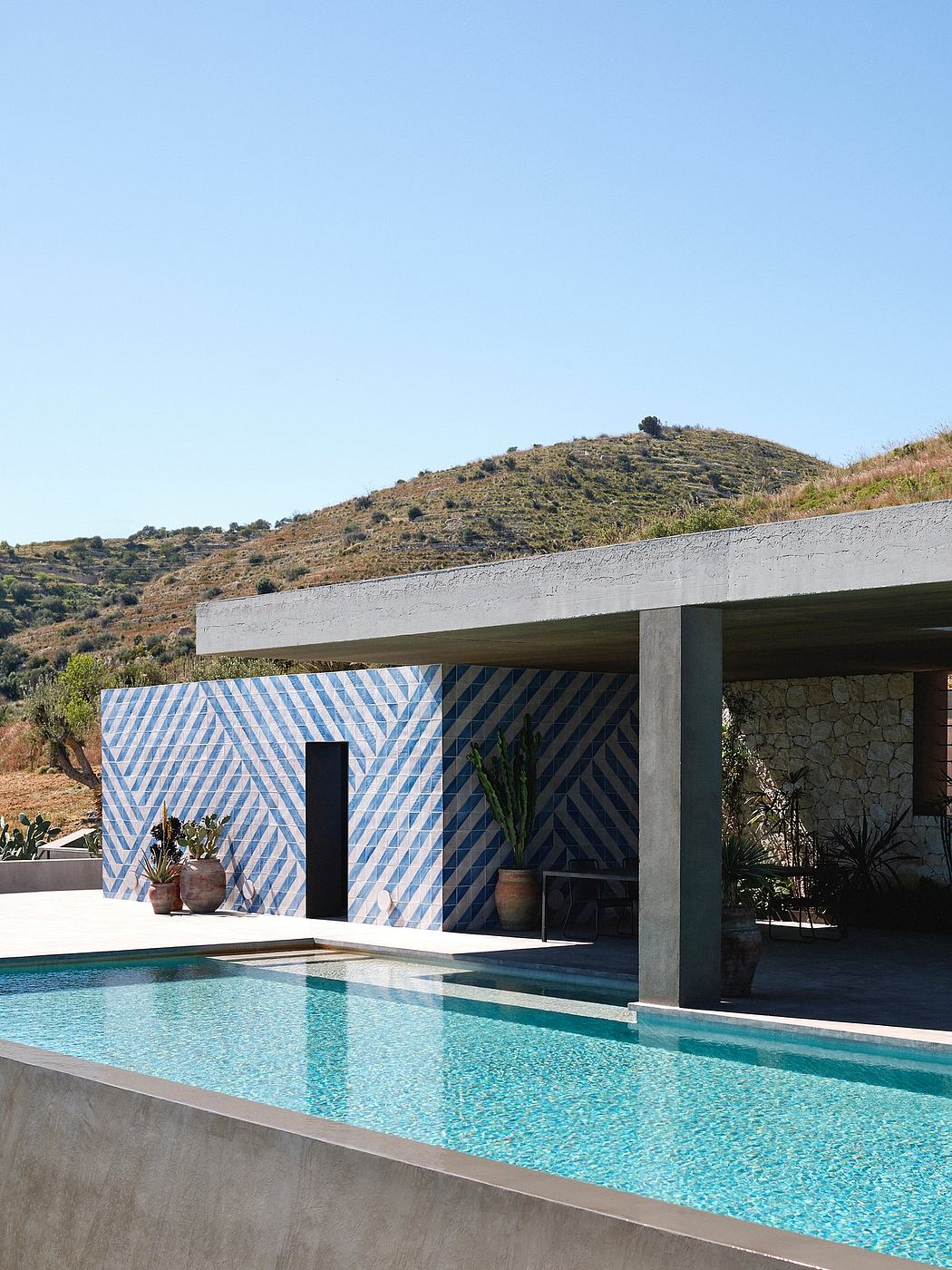 Contemporary poolside with geometric wall design and hillside view.