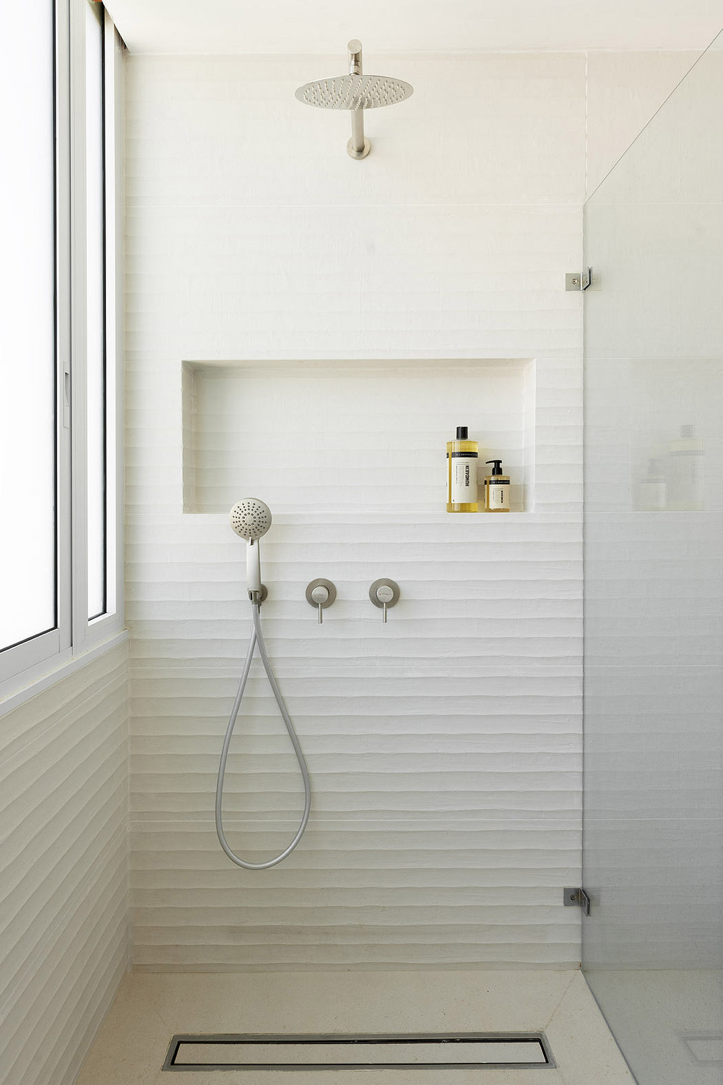Modern white tiled shower with rainfall and handheld showerheads.