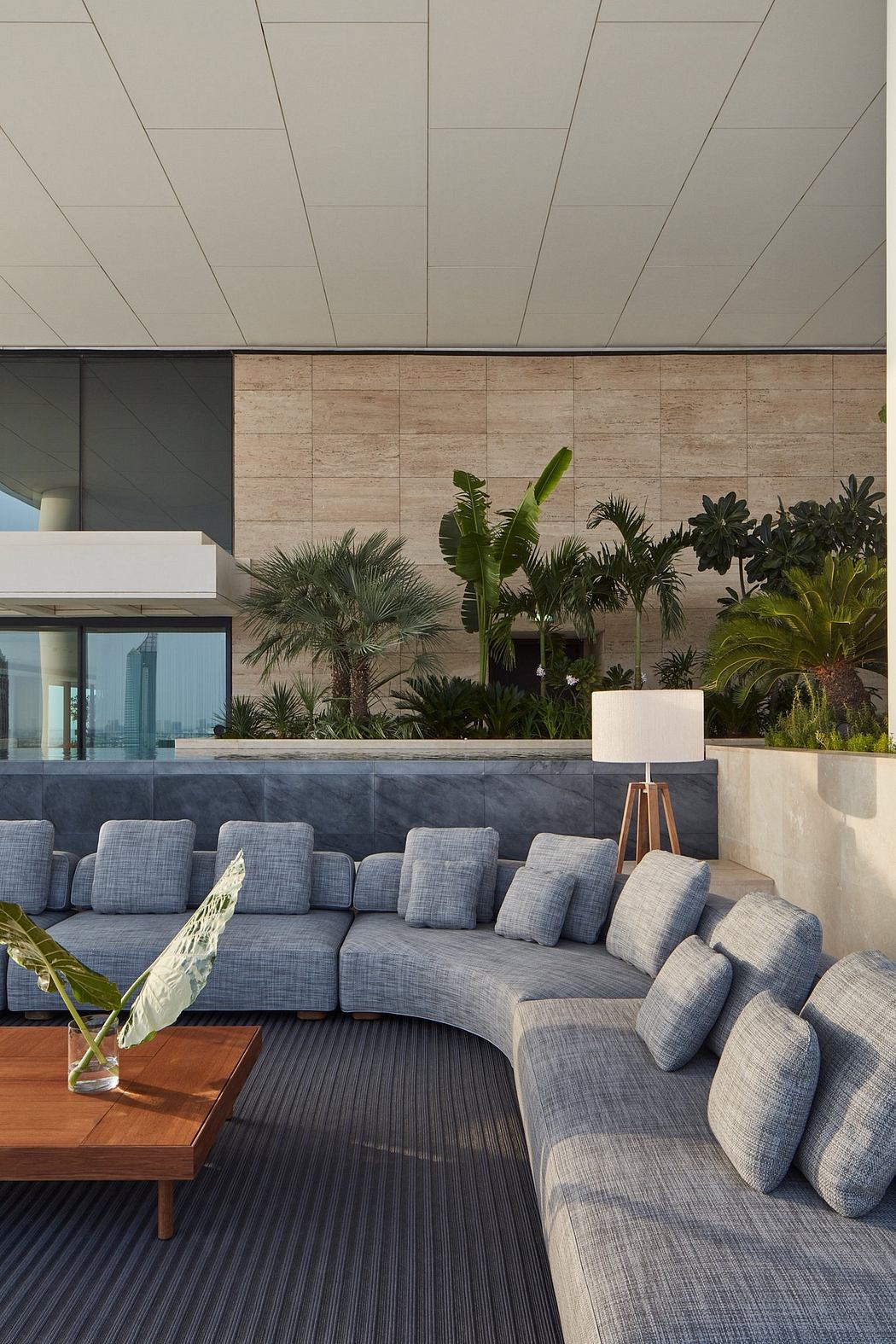 A modern, open-concept space with lush tropical plants, a large gray sofa, and a wooden coffee table.