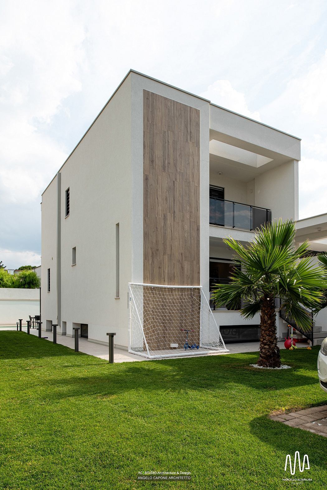 A modern, minimalist building with a wood-paneled facade, balcony, and lush landscaping.