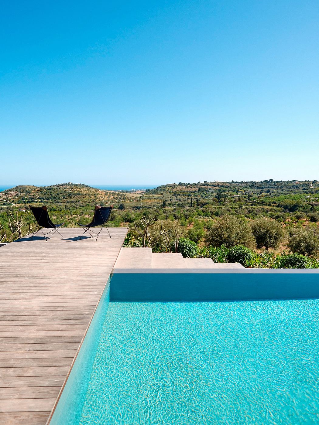 Contemporary infinity pool overlooking a scenic landscape with lounge chairs.