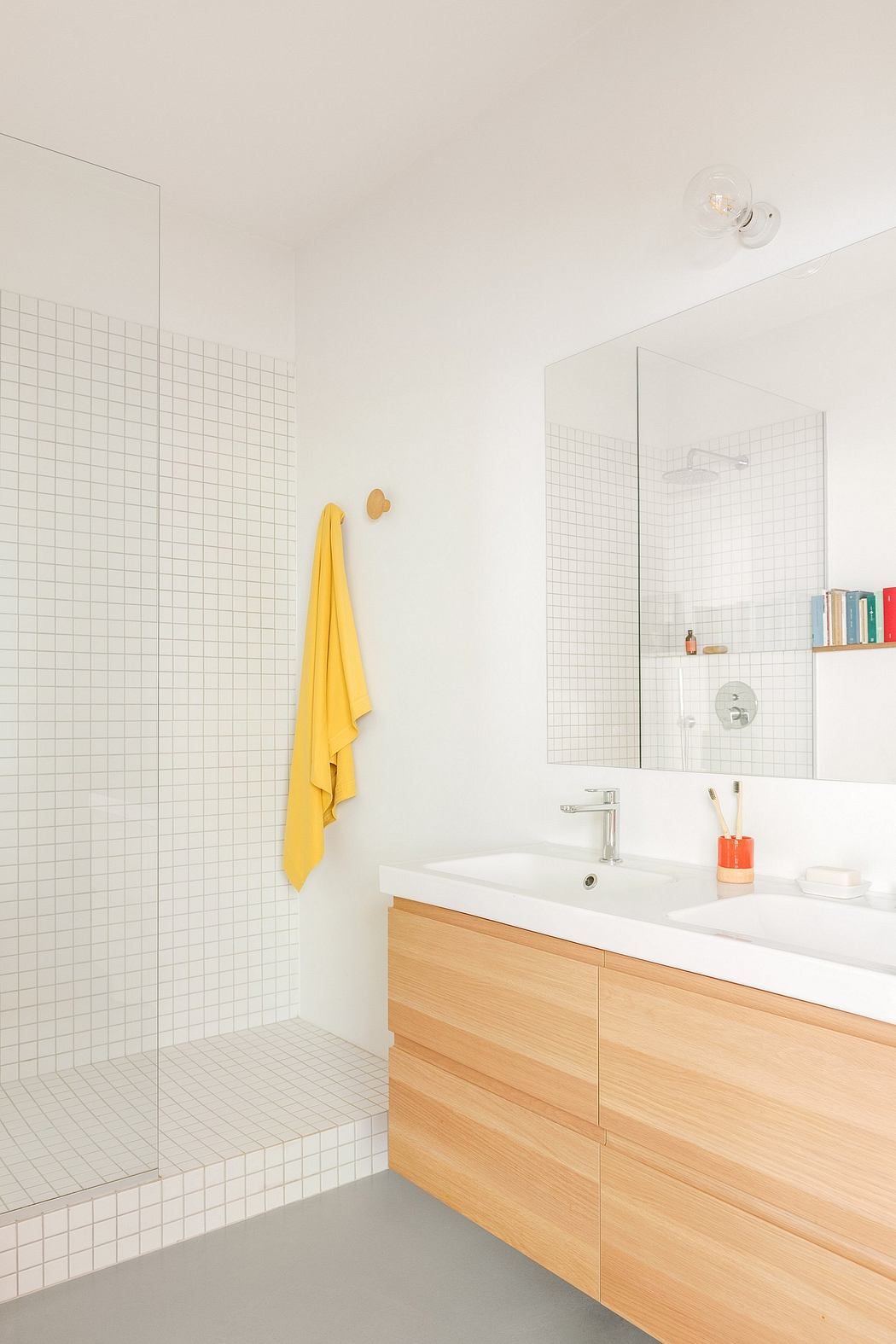 Minimalist bathroom with white tiles, wooden vanity, and a yellow towel.