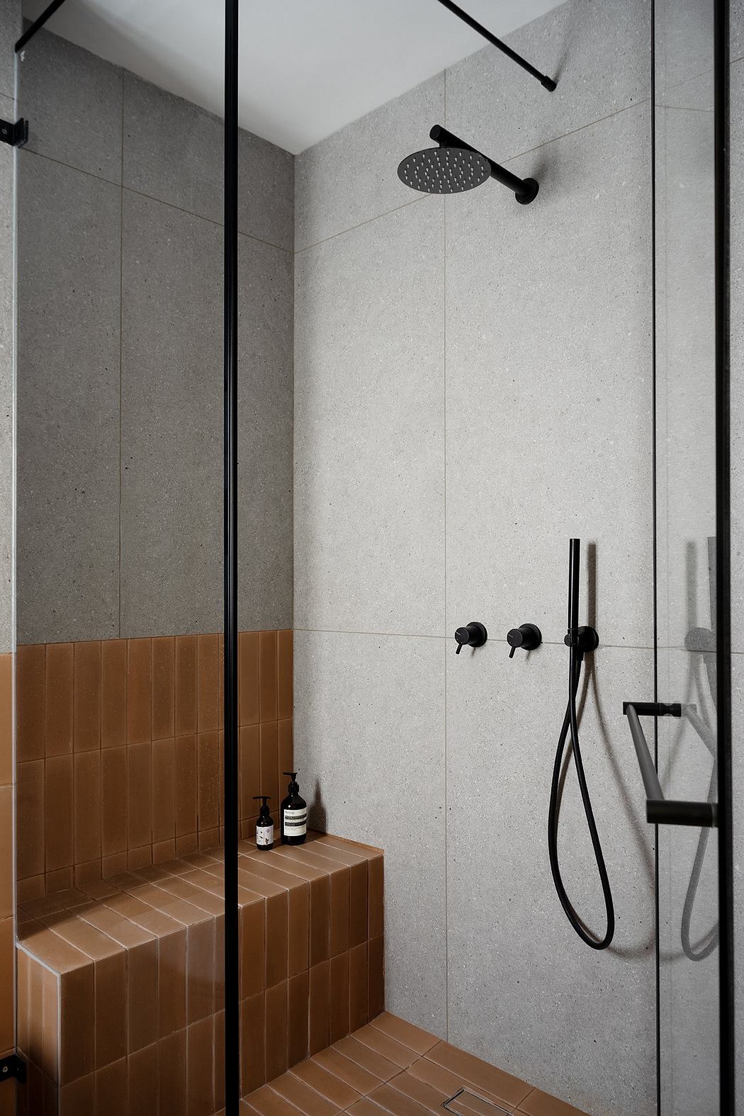 Modern shower with gray walls, brown tiles, and black fixtures.