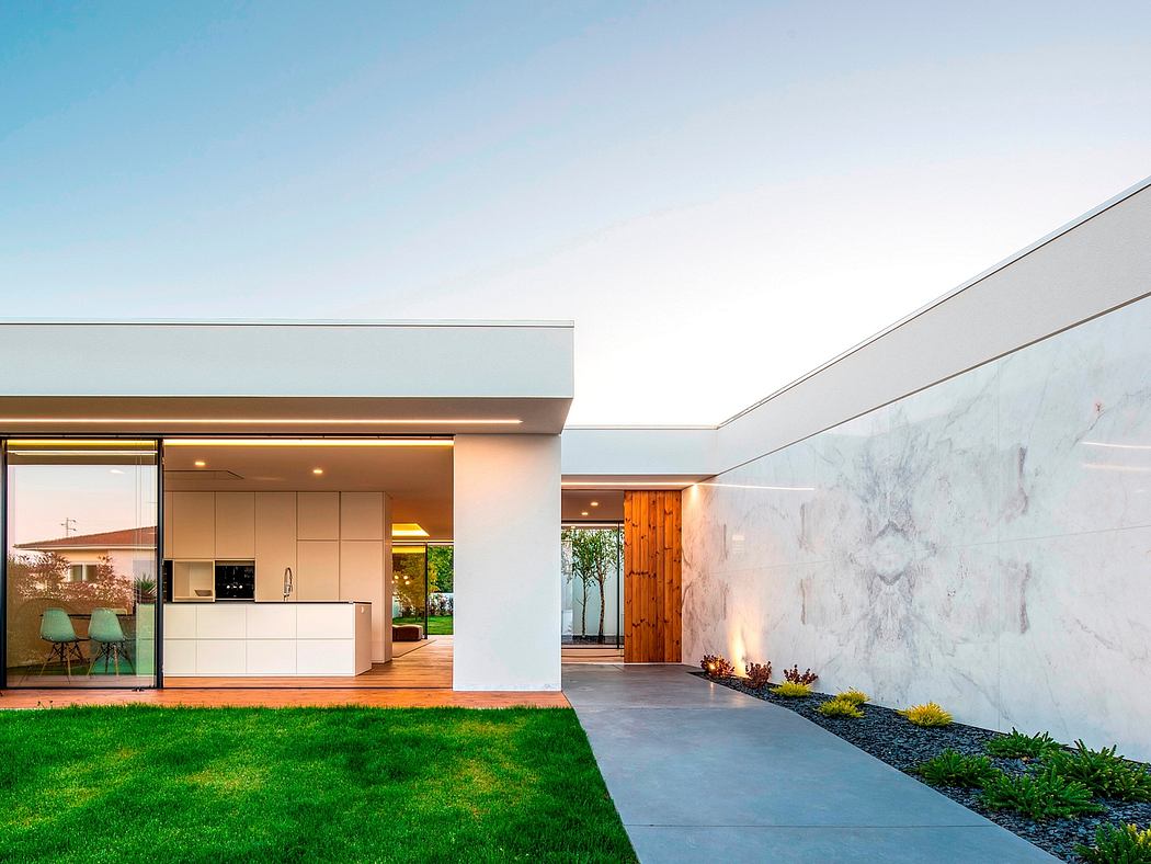 Modern home exterior with clean lines, glass walls, and lush lawn.