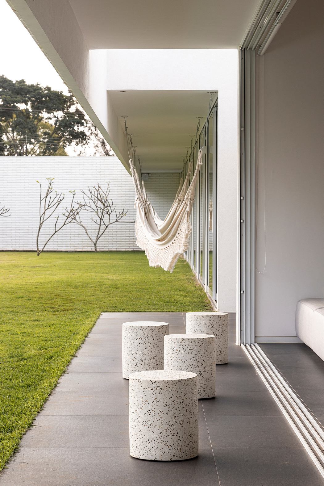 Tranquil outdoor patio with hammock, concrete stools, and expansive green lawn.