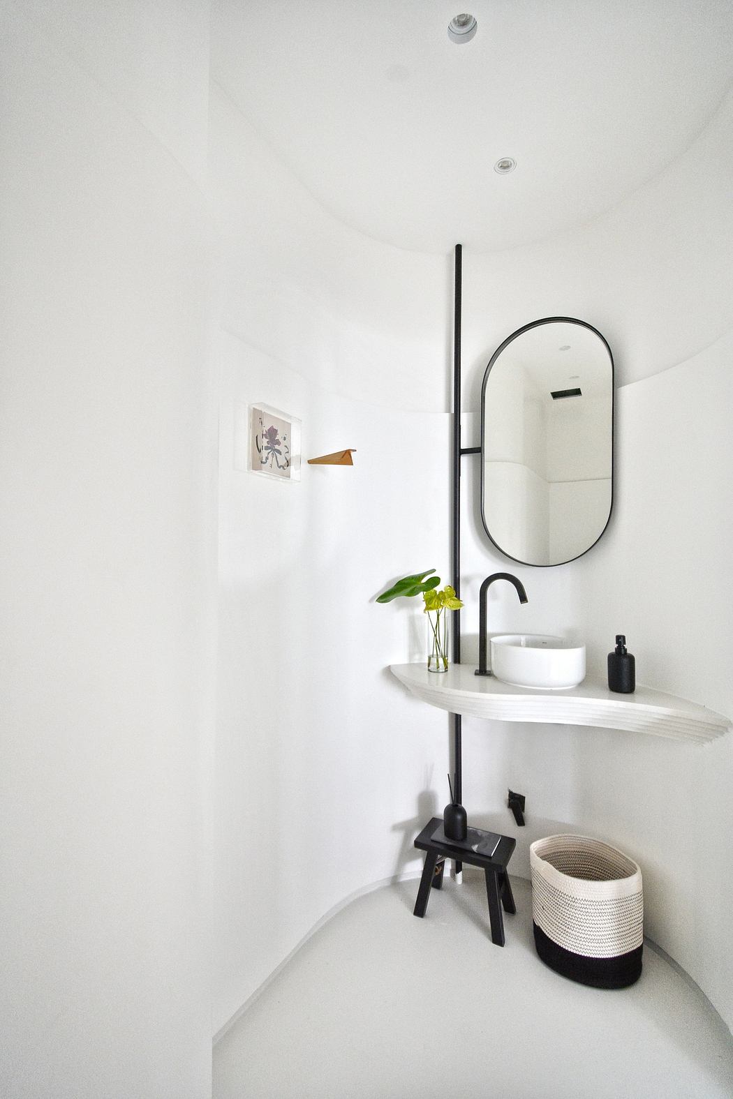 Modern minimalist bathroom with sleek black fixtures, oval mirror, and potted plant.
