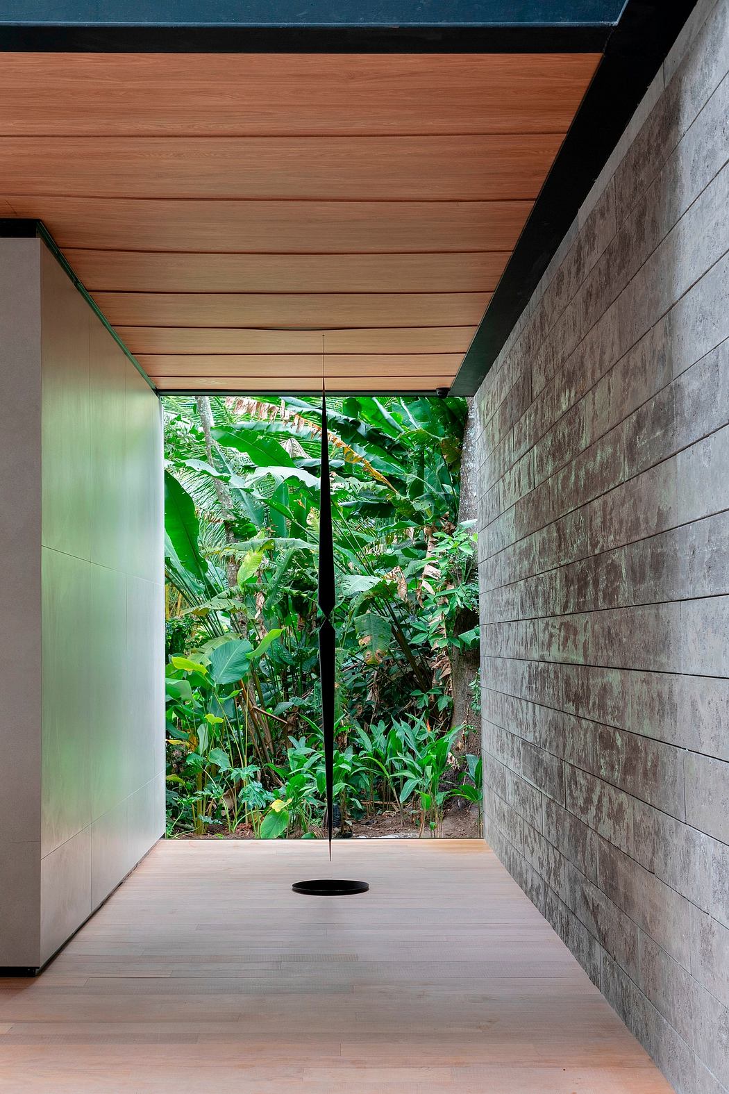Sleek corridor with wooden ceiling, concrete walls, and tropical garden view.