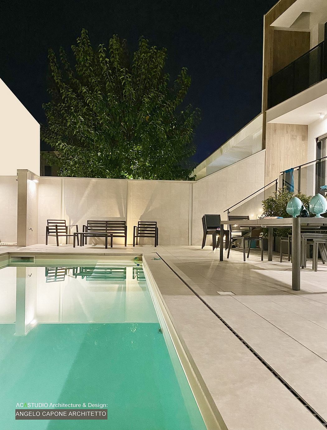 Sleek modern patio with pool, dining area, and lush greenery overhead.