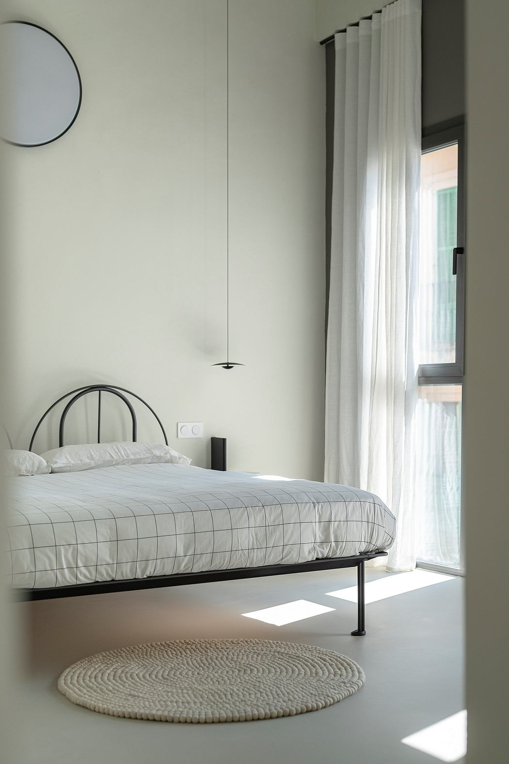 Minimalist bedroom with white walls, sheer curtains, and round mirror.