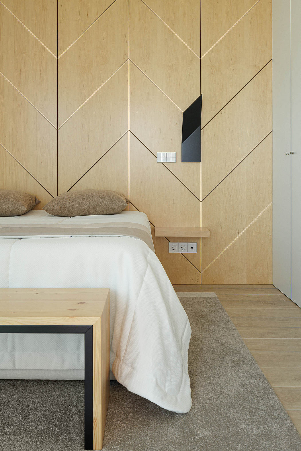 Minimalist bedroom with geometric wooden paneling and accent wall, clean lines, and simple furnishings.