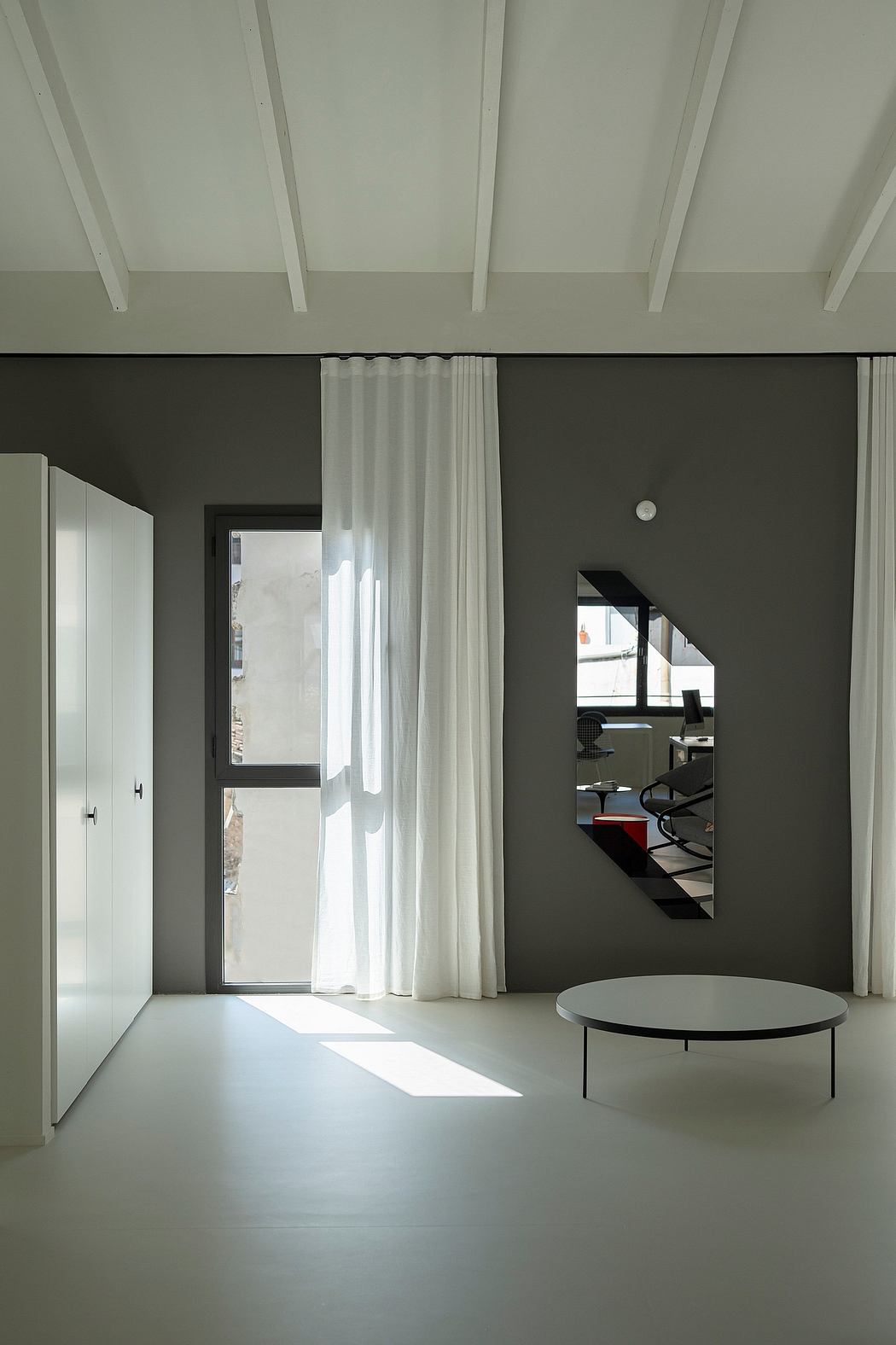 Minimalist interior with white beams, sheer curtains, and a central table.
