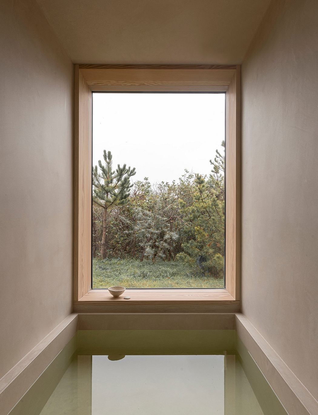A minimalist window with a view of greenery and a small bowl on the sill