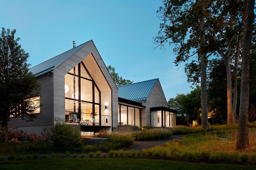 Modern house with large windows illuminated at dusk surrounded by trees.