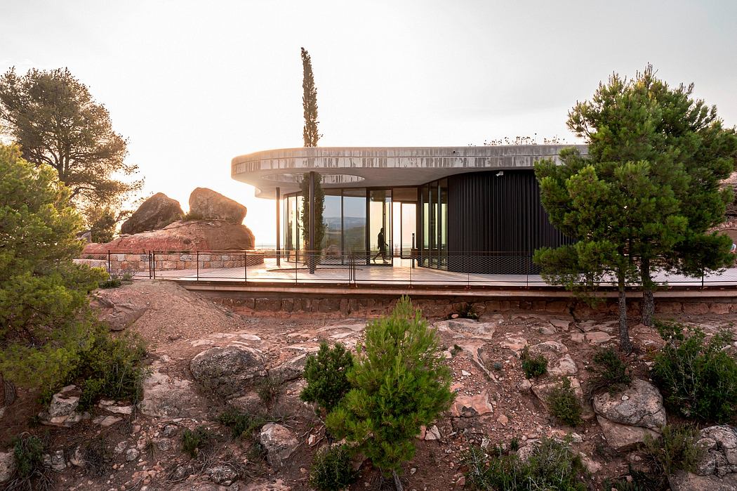 Modern circular house with glass walls surrounded by trees at dusk.