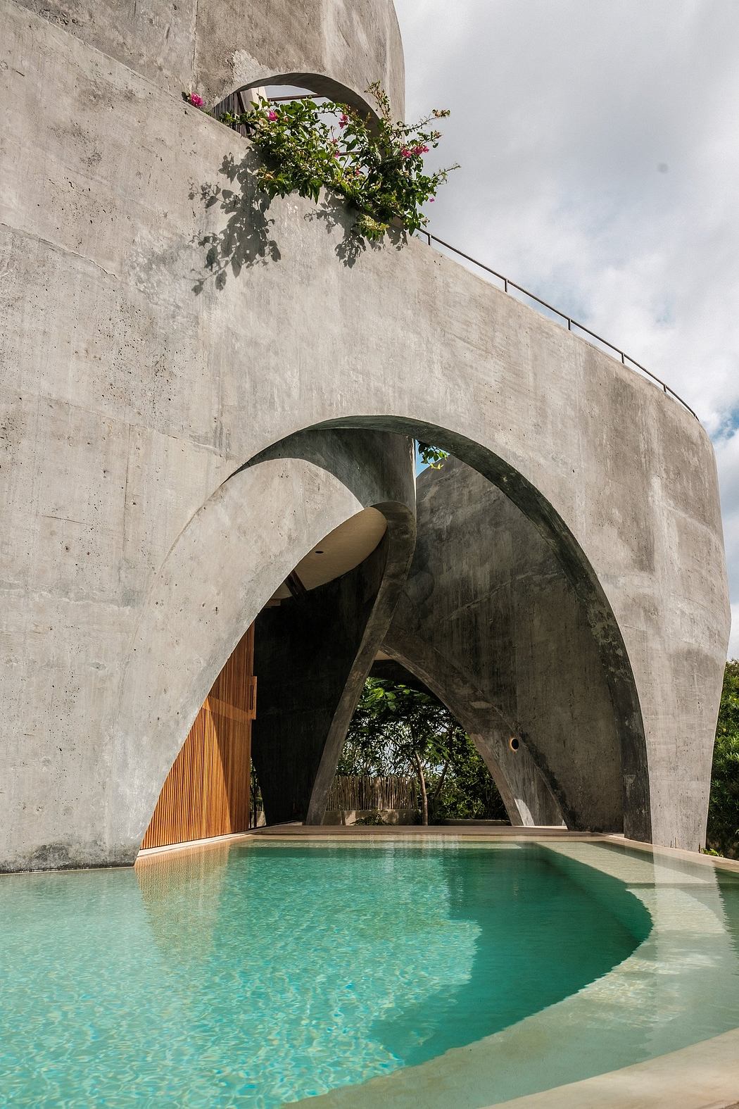 Striking arched concrete structure with a vibrant green swimming pool beneath.