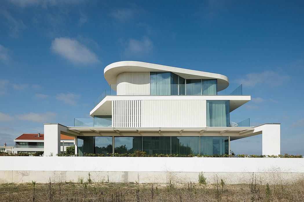 A modernist beachfront villa with a curved roofline, expansive glass walls, and a balcony.