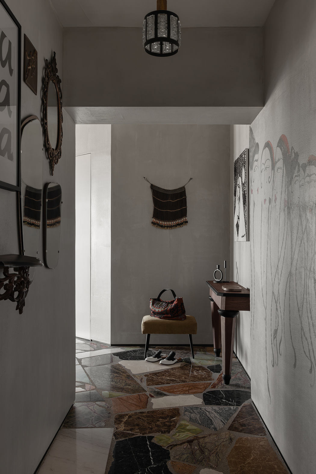 Moody, minimalist hallway with rustic stone flooring, hanging artwork, and a cozy bench.