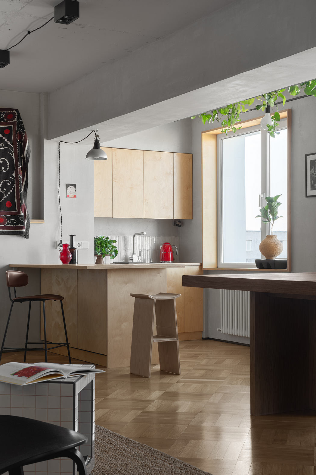 Minimalist kitchen with wooden cabinetry, window with potted plants, and industrial-style lighting.
