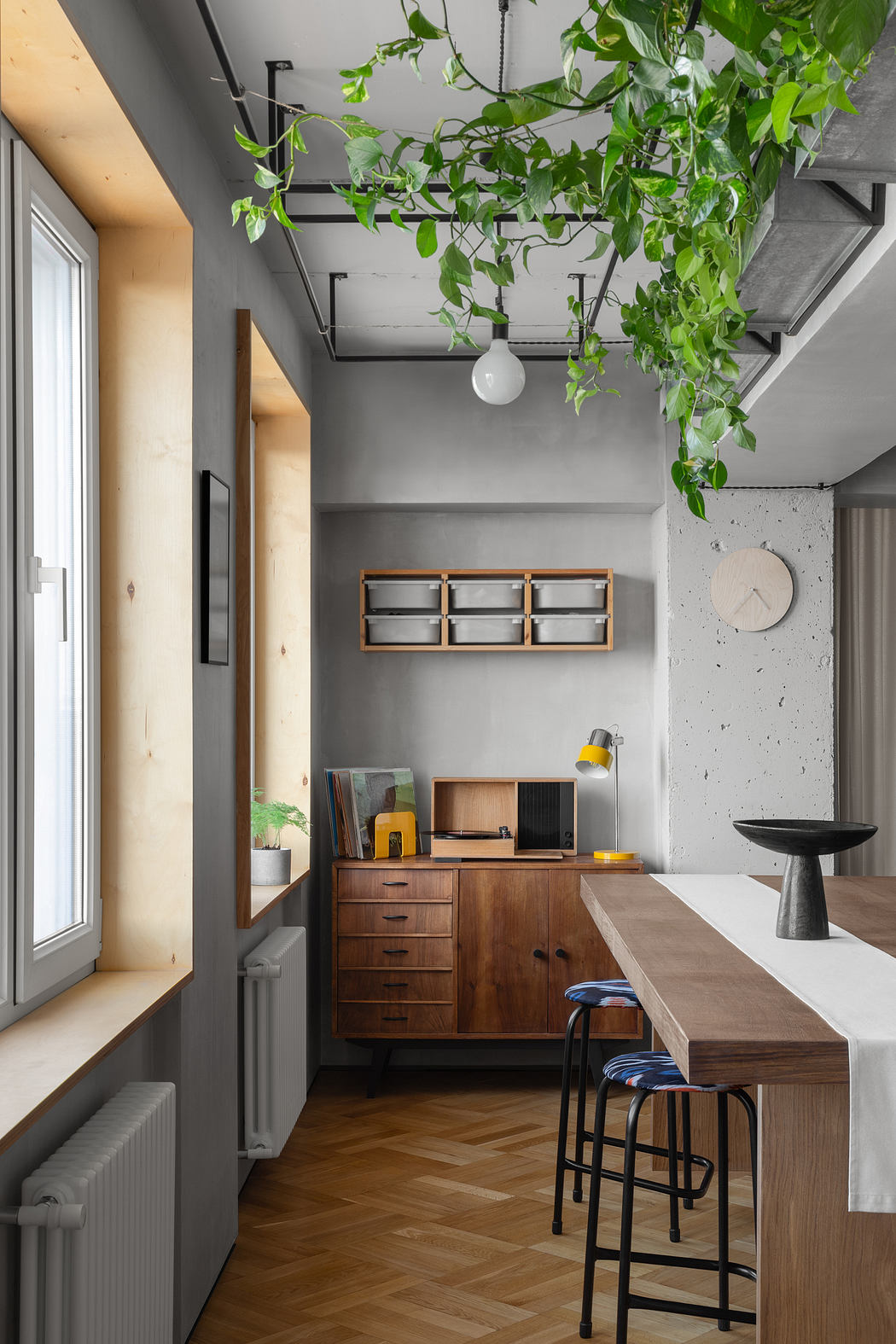 Modern industrial-style kitchen with wooden cabinets, hanging plants, and textured concrete walls.