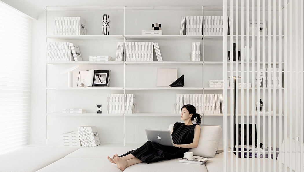 A modern, minimalist living space with floor-to-ceiling shelves, a plush chair, and a laptop.