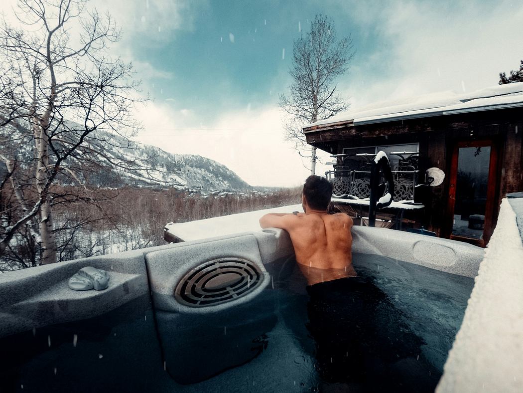 Person in outdoor hot tub by a winter landscape.
