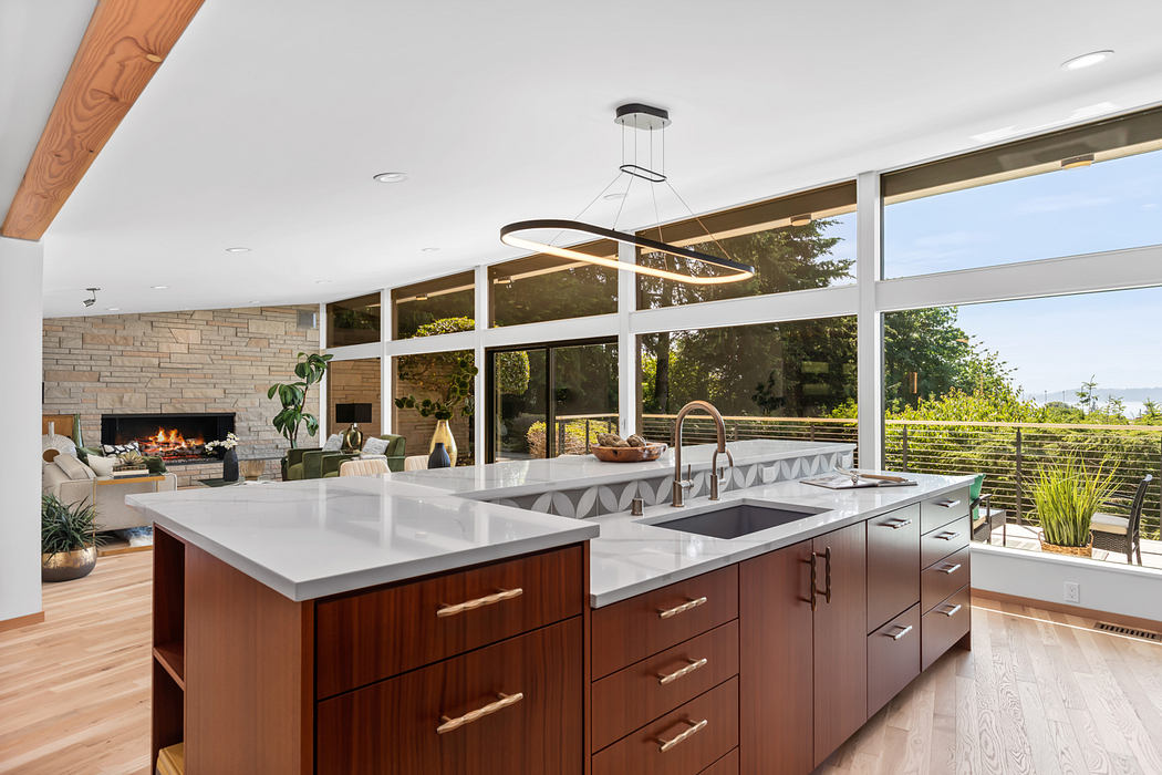 Modern open-concept kitchen with wood and stone accents, large windows, and a fireplace.