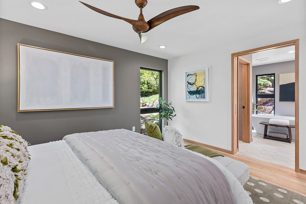 Spacious bedroom with large framed artwork, ceiling fan, and wooden furniture.
