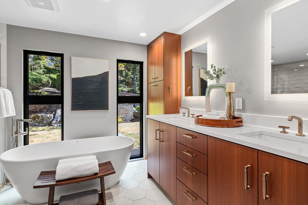 A modern bathroom with sleek wood cabinetry, a freestanding bathtub, and nature-inspired artwork.