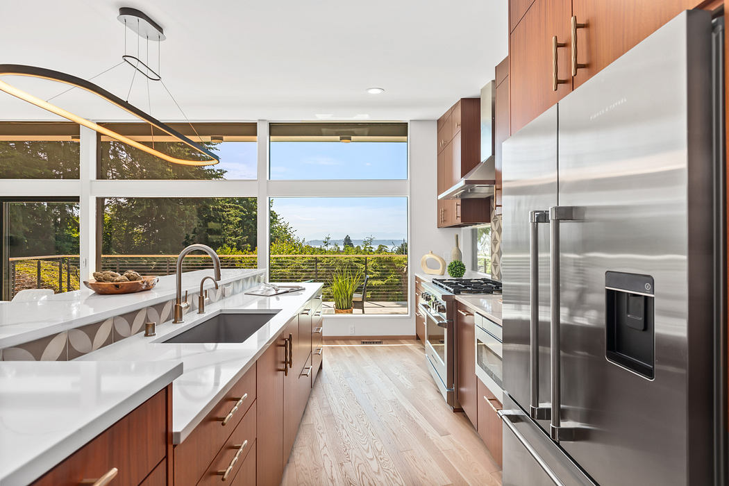 Large modern kitchen with floor-to-ceiling windows offering scenic views, sleek appliances and cabinetry.