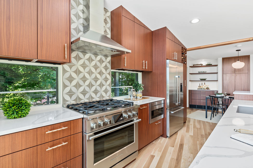 Sleek, modern kitchen with wood cabinets, geometric tiled backsplash, and stainless steel appliances.