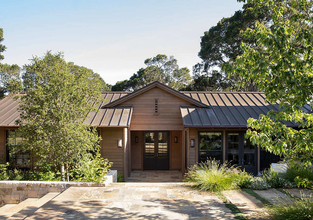 A two-story, wooden-clad home with a gabled roof and large windows overlooking a wooded area.