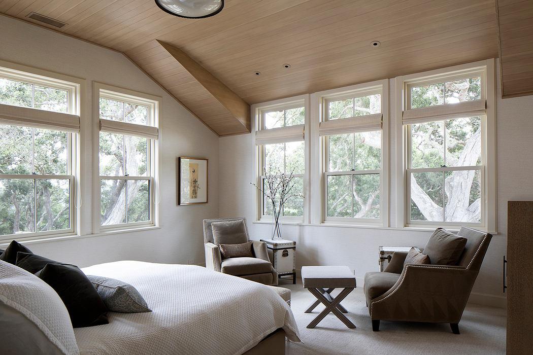 Spacious bedroom with vaulted ceiling, large windows, and cozy seating area.